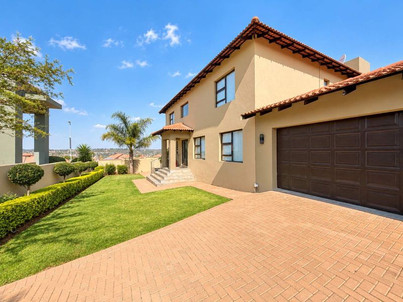A well-maintained double-story house featuring a paved driveway, double garage, and a neat, landscaped front garden under a clear blue sky.