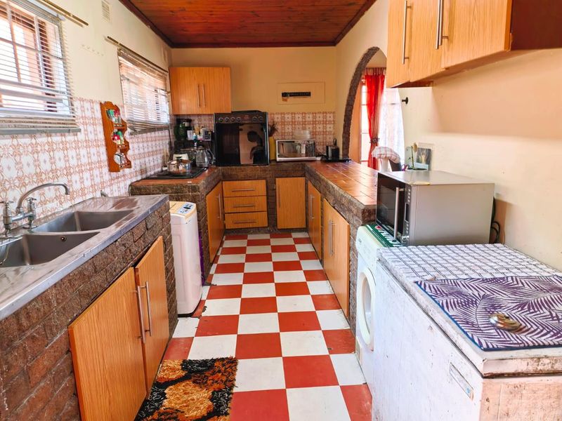 A dated kitchen featuring brick-built cabinetry, a double basin sink, tiled backsplash, and a wooden ceiling with a checkerboard floor pattern.