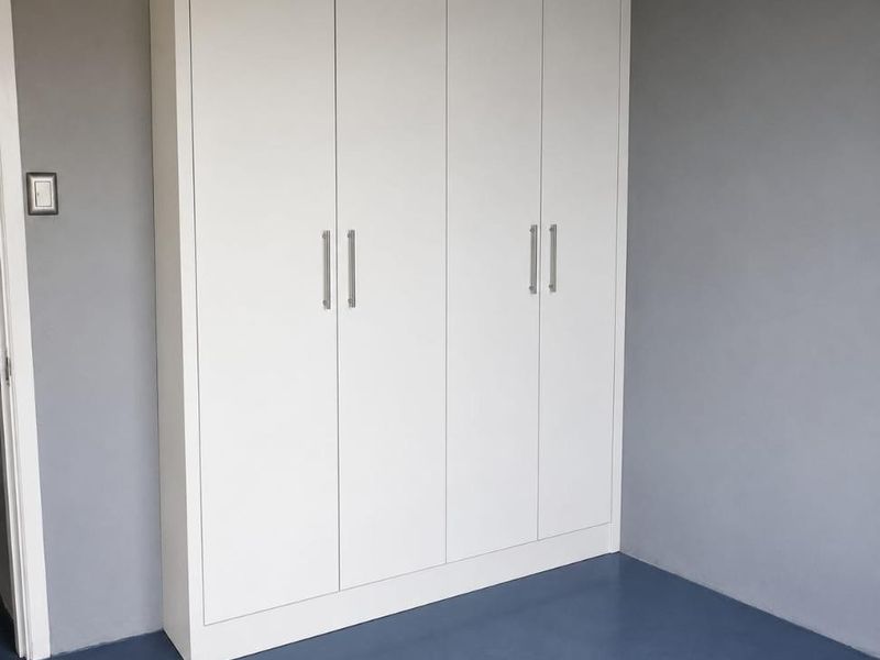 A clean bedroom interior featuring a modern, white built-in wardrobe with sleek handles against a neutral grey wall.