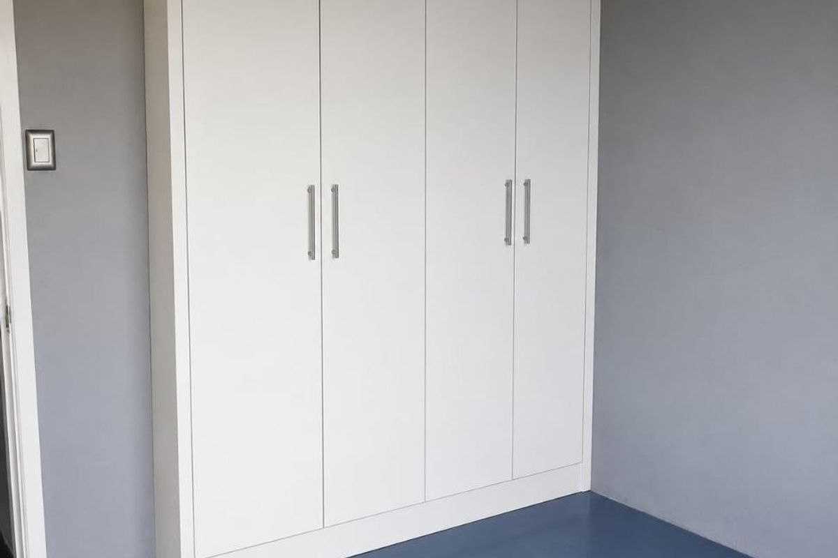 A clean bedroom interior featuring a modern, white built-in wardrobe with sleek handles against a neutral grey wall.