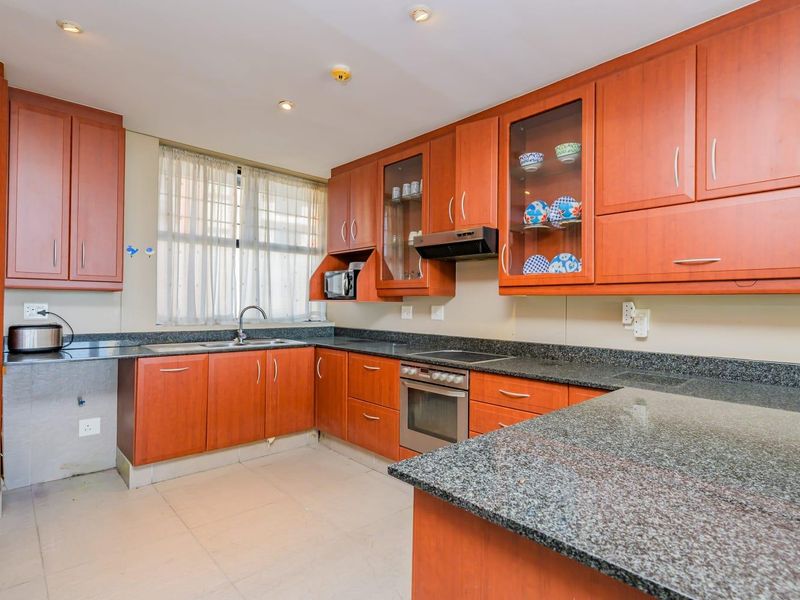 A functional kitchen featuring cherry wood cabinetry, granite countertops, a built-in oven, and an electric hob with an extractor fan.