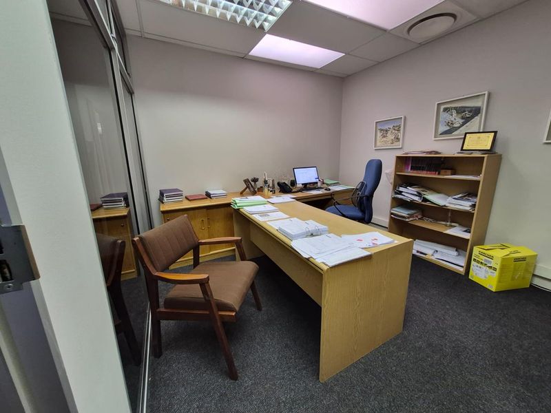 A functional office space featuring a glass partition wall, carpeted flooring, and a suspended ceiling with recessed lighting.