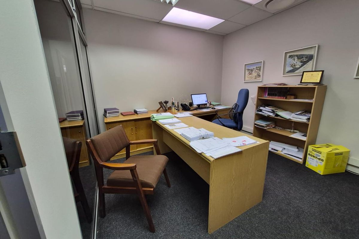 A functional office space featuring a glass partition wall, carpeted flooring, and a suspended ceiling with recessed lighting.