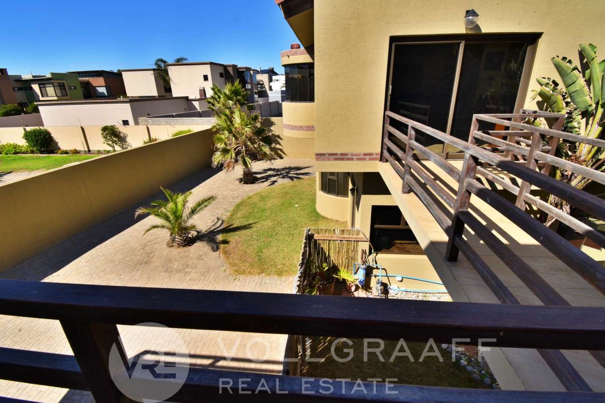 Elevated view from a balcony overlooking a private rear garden with paved areas, lawn, and perimeter boundary walls.