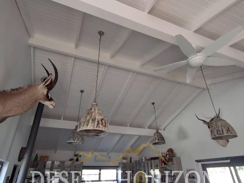 Open plan living and kitchen area featuring high exposed beam ceilings, modern cabinetry, and a central fireplace, creating a spacious and airy atmosphere.