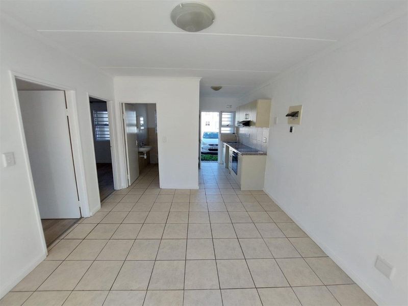 An open-plan living and kitchen area featuring tiled flooring, built-in cabinetry, and integrated cooking appliances, leading to an exterior entrance.