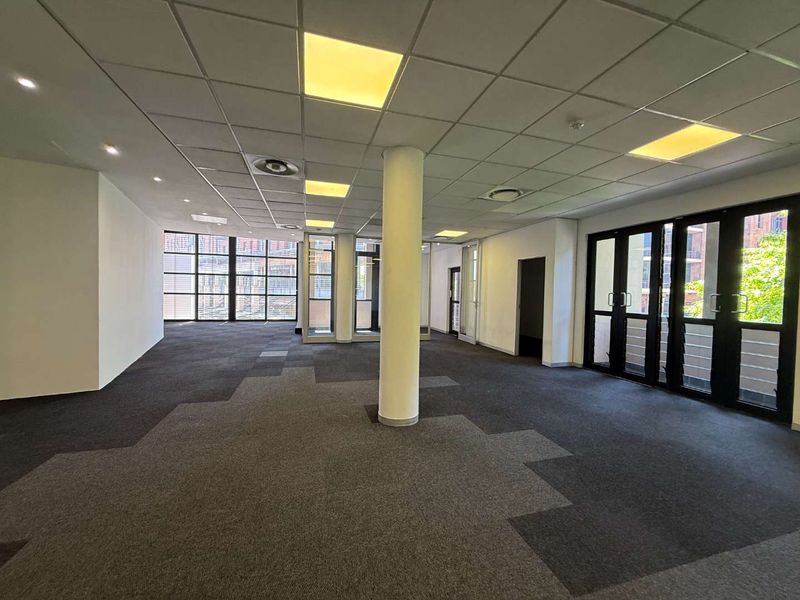 Spacious, open-plan office area featuring a suspended ceiling, recessed lighting, central air conditioning, and large windows providing ample natural light.