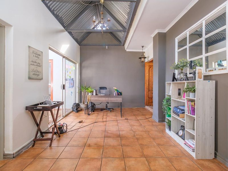 A home office space featuring a unique vaulted corrugated metal ceiling, ceramic tile flooring, and a sliding glass door providing natural light.