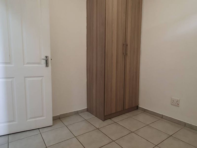 A clean, empty bedroom featuring neutral tiled flooring and a built-in wooden wardrobe, offering a blank canvas for personalization.