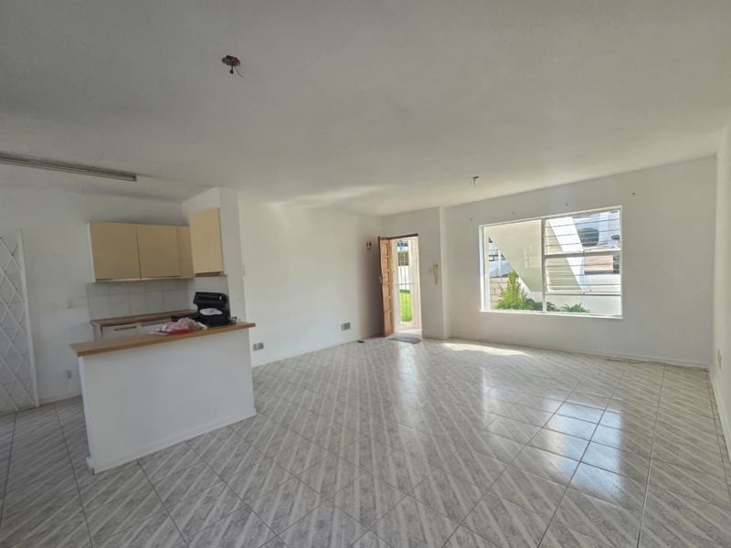 An open-plan living and kitchen area featuring tiled flooring, neutral walls, and a breakfast counter, offering a blank canvas for renovation.