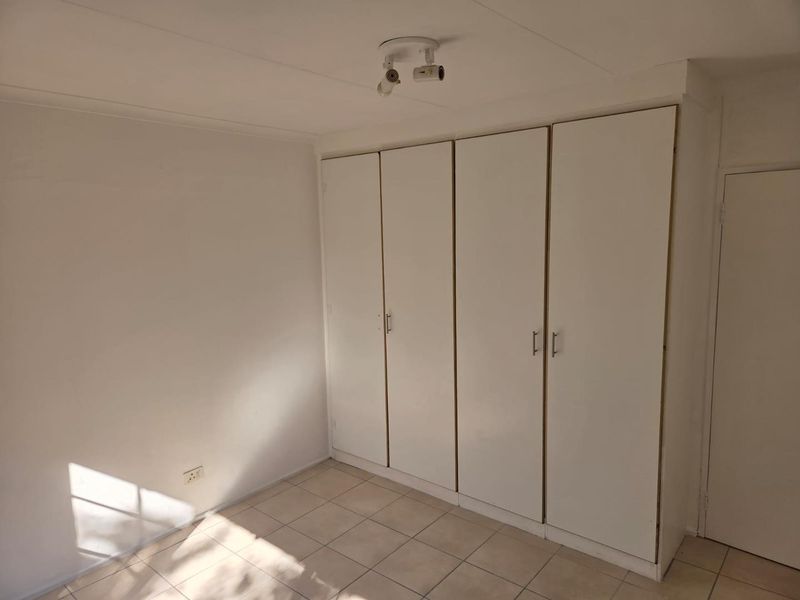 A bright, empty bedroom featuring neutral tiled flooring and ample built-in cupboard storage space.