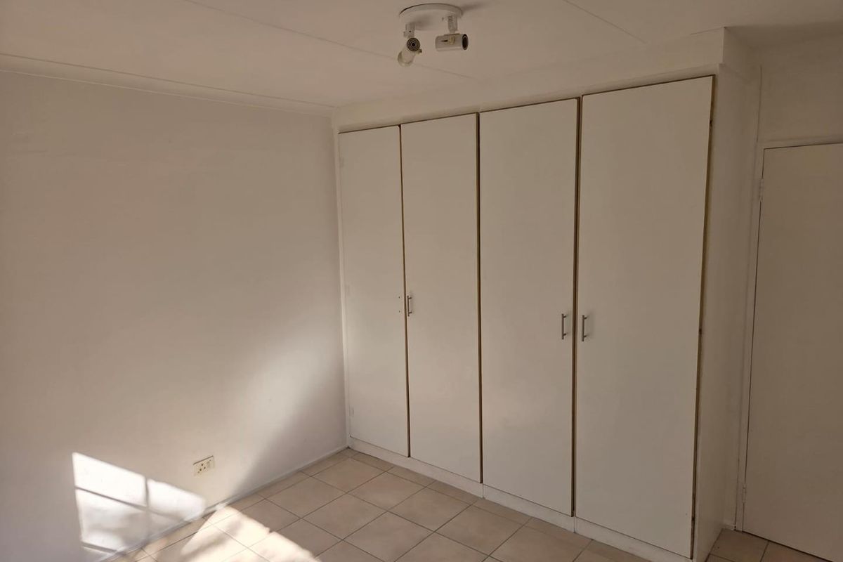A bright, empty bedroom featuring neutral tiled flooring and ample built-in cupboard storage space.