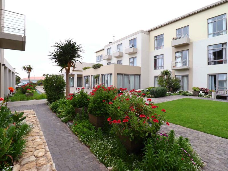 A well-maintained apartment complex exterior featuring a landscaped garden, paved walkways, and private balconies with sliding glass doors.