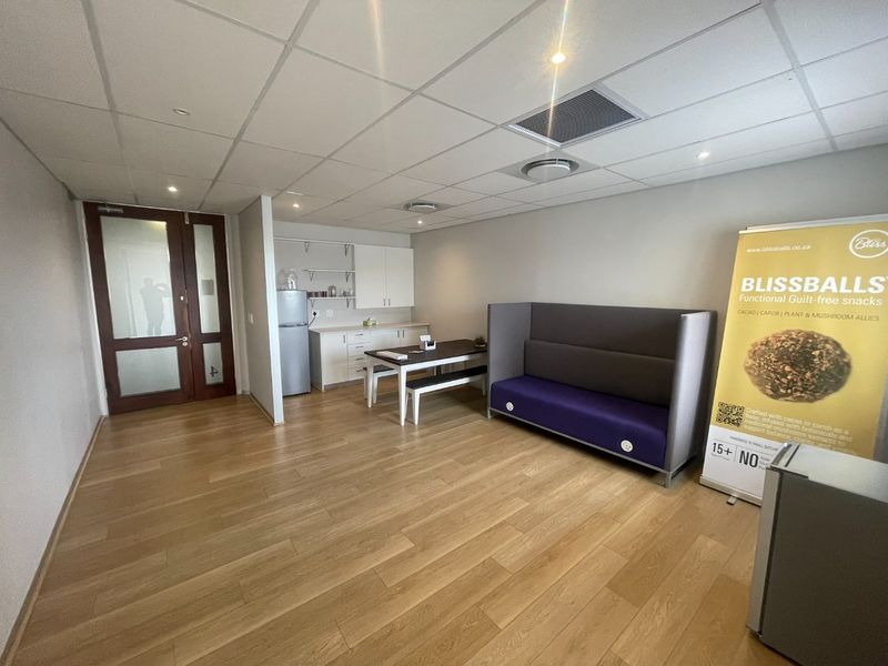 A modern office space featuring a suspended ceiling, recessed lighting, laminate flooring, and a compact built-in kitchenette area.