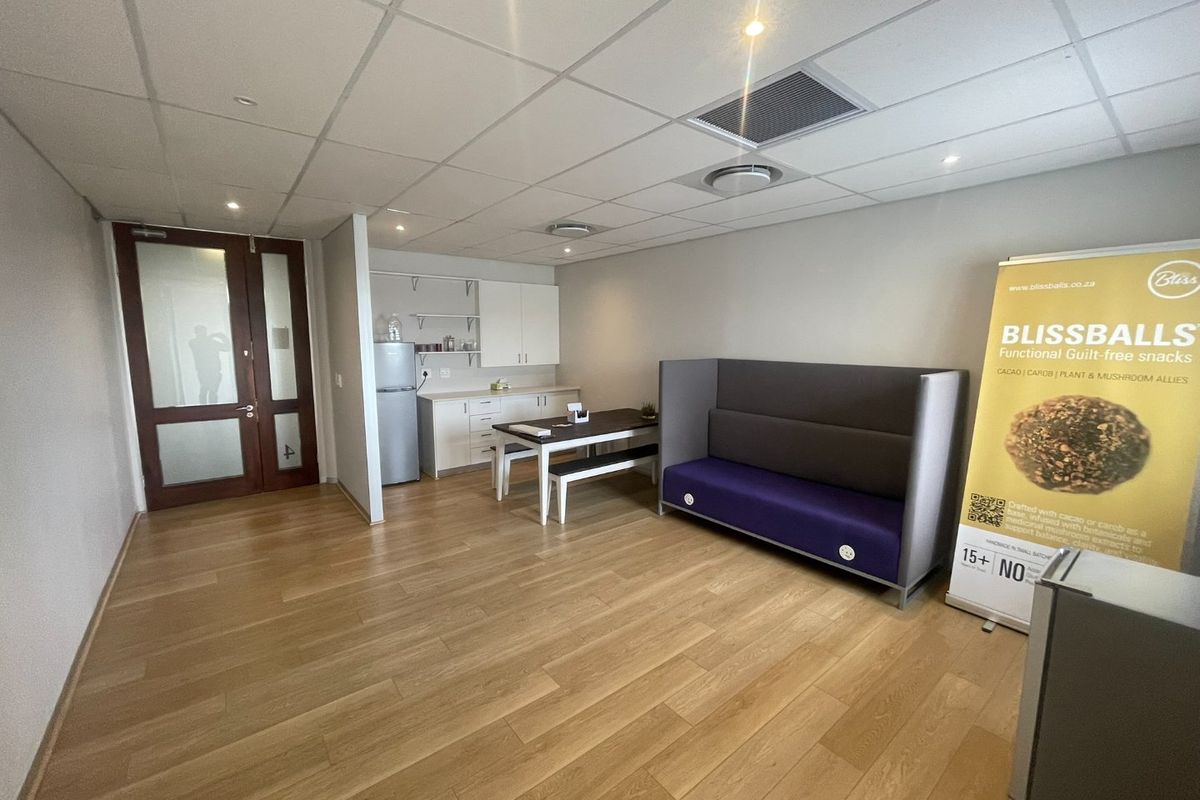 A modern office space featuring a suspended ceiling, recessed lighting, laminate flooring, and a compact built-in kitchenette area.