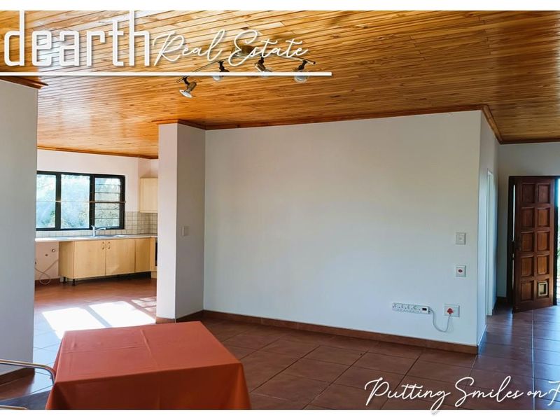 Spacious open-plan living area featuring a warm timber ceiling, ceramic tiled flooring, and an adjoining kitchen with built-in cabinetry.