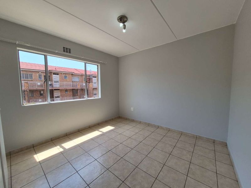 A bright, empty bedroom featuring neutral wall paint, tiled flooring, and a large window providing natural light.