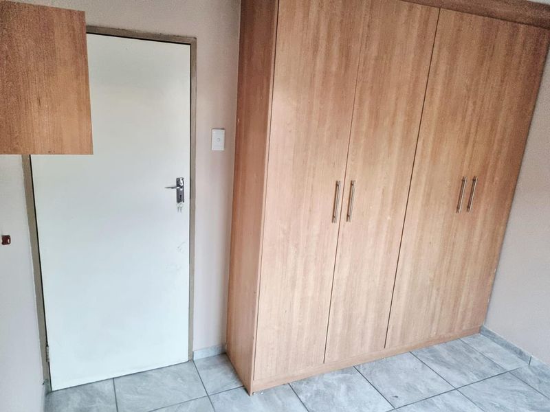 A bedroom featuring tiled flooring and a large built-in wooden wardrobe with ample storage space.