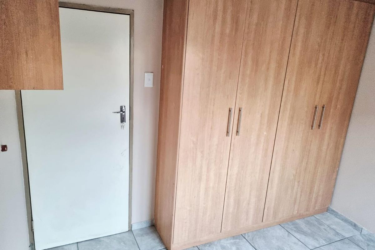 A bedroom featuring tiled flooring and a large built-in wooden wardrobe with ample storage space.