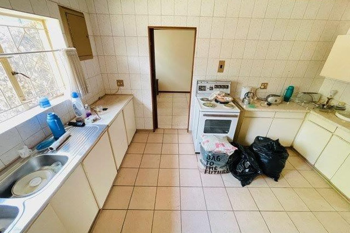 A dated kitchen featuring tiled walls and flooring, built-in cabinetry, and a freestanding stove, offering potential for a modern renovation.