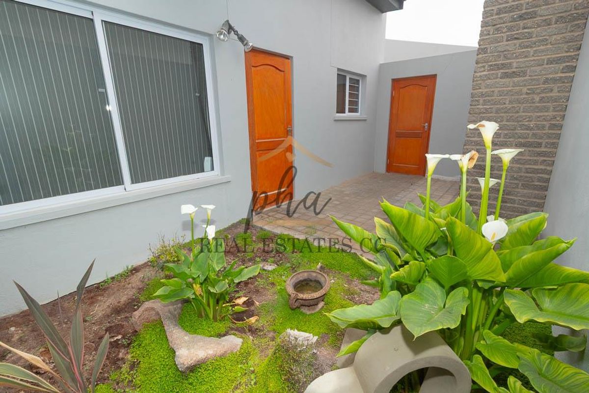 A neat rear courtyard area featuring paved flooring, established garden beds, and access to the home via sliding and standard wooden doors.