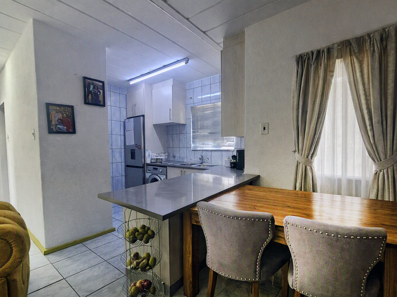 Open plan kitchen and dining area featuring tiled flooring, built-in cabinetry, a breakfast bar, and a window with curtains.