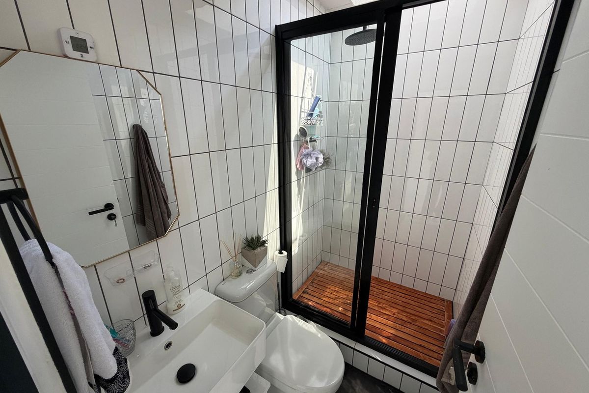 Modern bathroom featuring white subway-style wall tiles, a walk-in shower with black framing and wooden floor slats, and a contemporary wall-mounted basin.