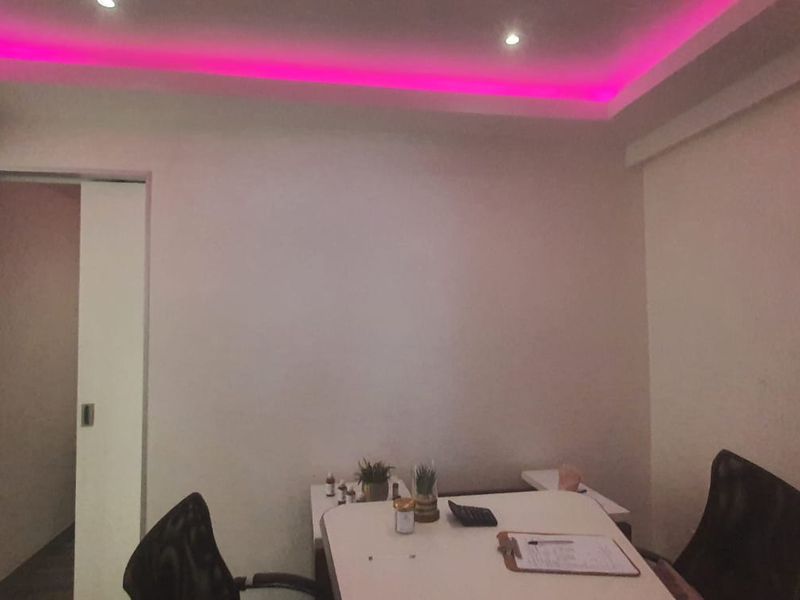 A functional office space featuring recessed ceiling lighting with integrated pink cove accent lighting and a sliding door entrance.