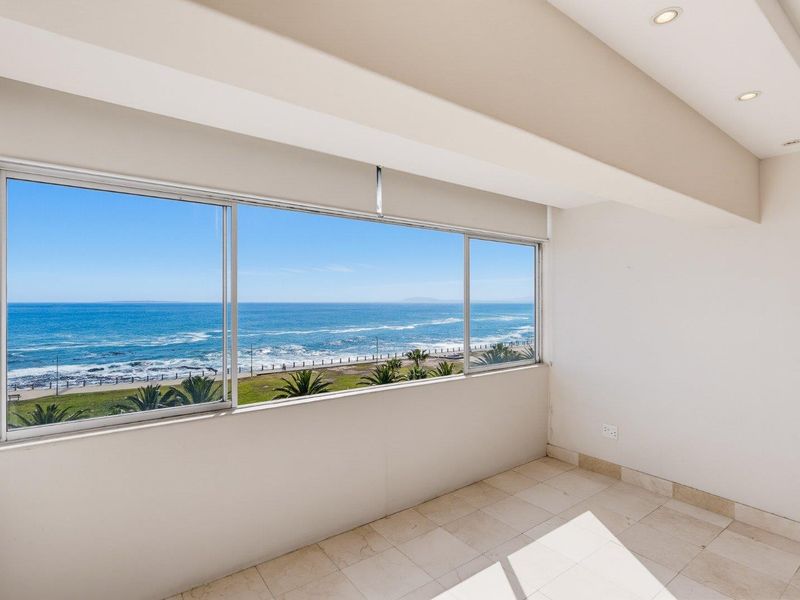An enclosed balcony featuring large sliding windows with expansive ocean views, tiled flooring, and recessed ceiling lighting.