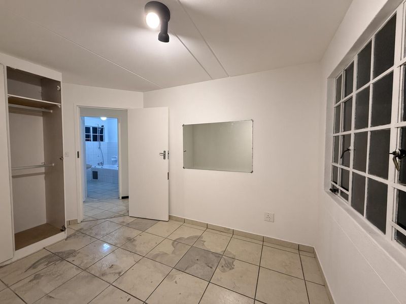 An empty bedroom featuring tiled flooring, a built-in wardrobe, and a wall-mounted mirror, with direct access to an adjoining bathroom.