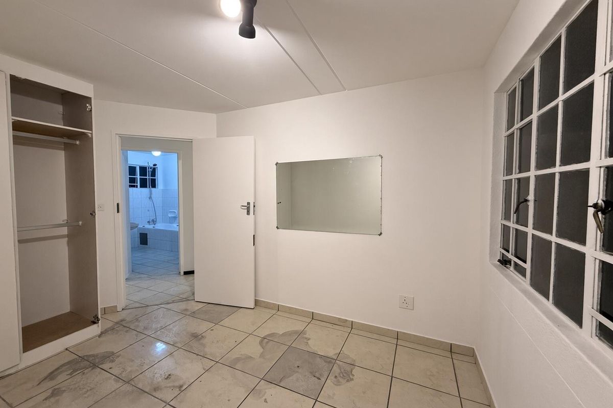 An empty bedroom featuring tiled flooring, a built-in wardrobe, and a wall-mounted mirror, with direct access to an adjoining bathroom.