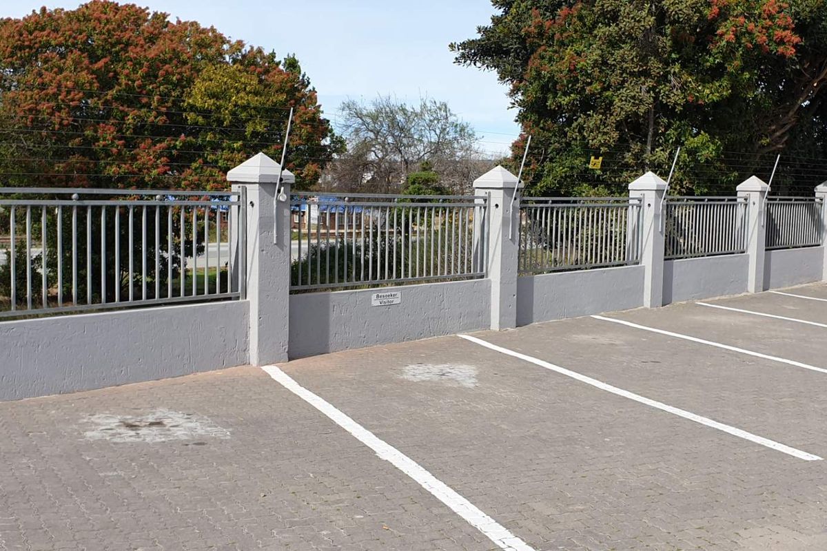A paved parking area featuring a secure perimeter wall with metal fencing and integrated electric security wiring.