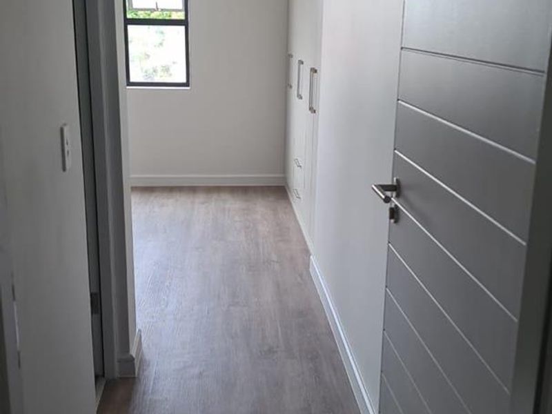 A clean, modern hallway featuring light-toned laminate flooring, built-in storage cupboards, and recessed ceiling lighting.