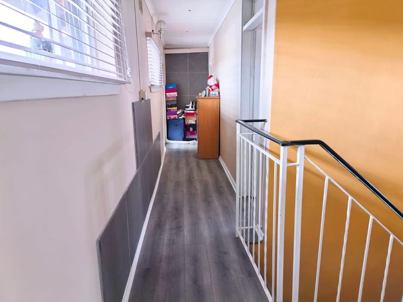 A functional hallway featuring laminate flooring, a metal balustrade, and wall-mounted lighting, providing access to adjacent rooms.