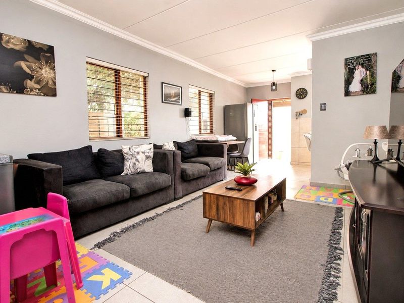 A well-lit living room featuring tiled flooring, coved ceilings, and large windows with venetian blinds, providing a comfortable and functional space.