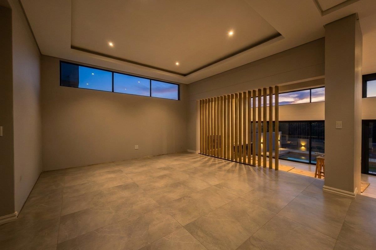 Spacious, modern living area featuring large format floor tiles, a decorative timber slat divider, recessed ceiling lighting, and expansive glass doors leading outdoors.