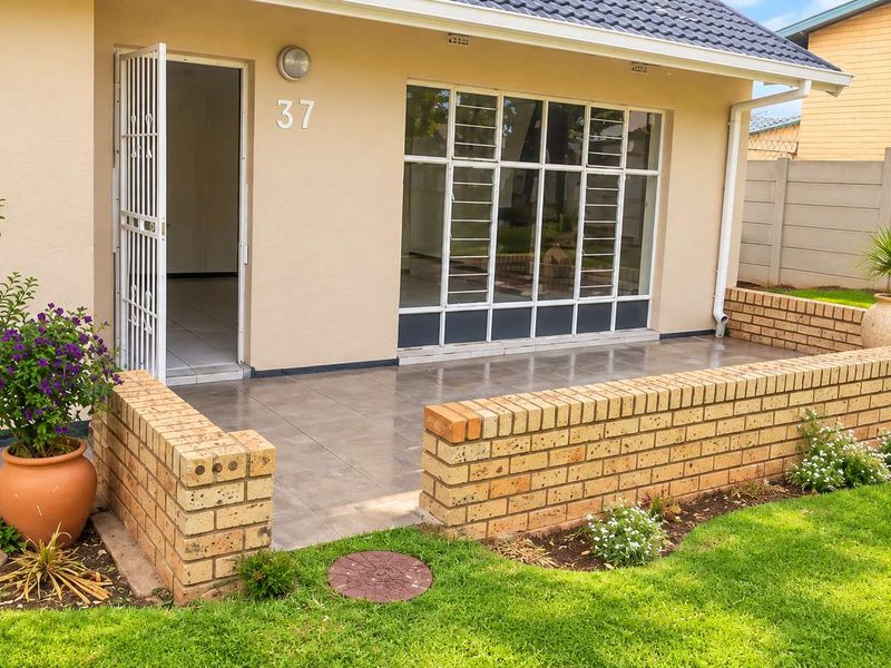 Front entrance of the house featuring a tiled patio, face brick boundary wall, and secure access point with large windows.