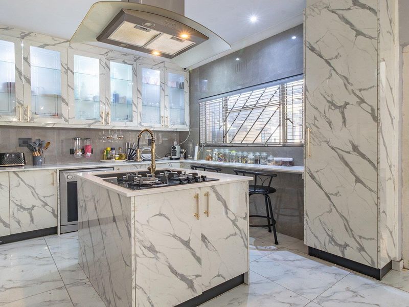 Modern kitchen featuring marble-look cabinetry, a central island with a gas cooktop, integrated extractor fan, and sleek tiled flooring throughout.