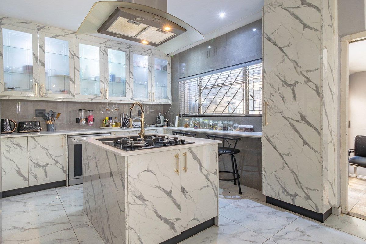 Modern kitchen featuring marble-look cabinetry, a central island with a gas cooktop, integrated extractor fan, and sleek tiled flooring throughout.