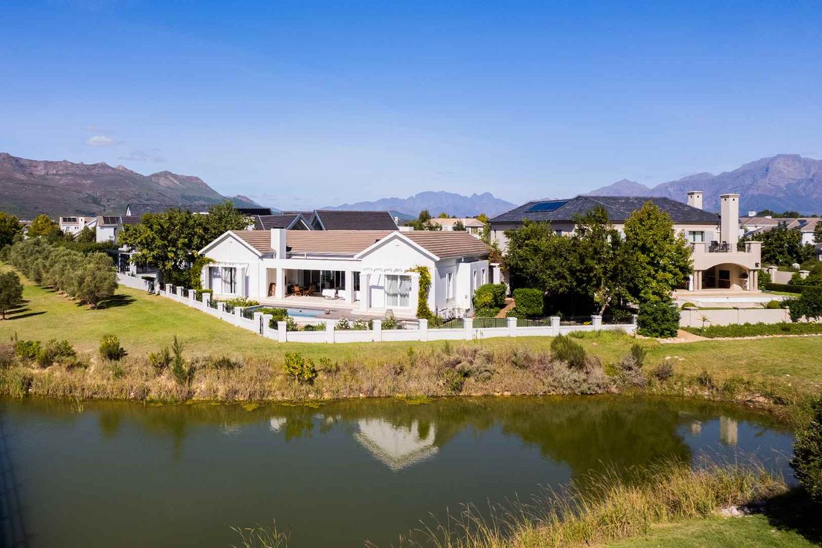 Aerial view of a well-maintained residential property featuring a swimming pool, patio, and landscaped garden, situated in a scenic estate setting.