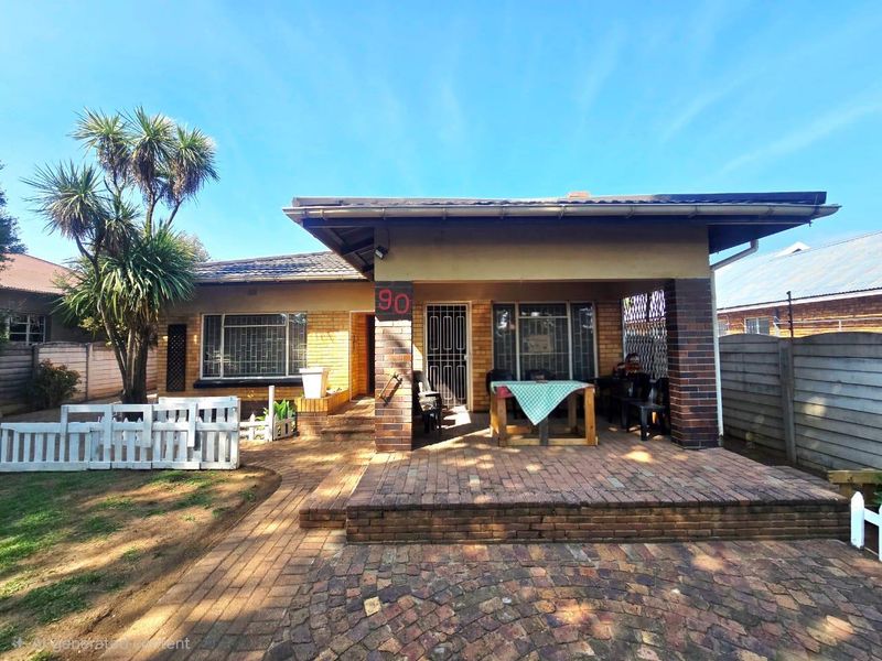 Front view of a brick house featuring a covered patio, paved entrance area, and established garden.