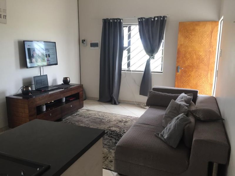 Open plan living area featuring tiled flooring, a window with security bars, and a solid wooden door.