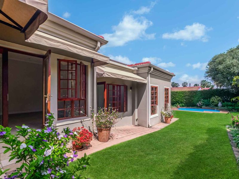 A well-maintained rear exterior featuring a paved patio with retractable awnings, timber windows, a lush green lawn, and a private swimming pool.
