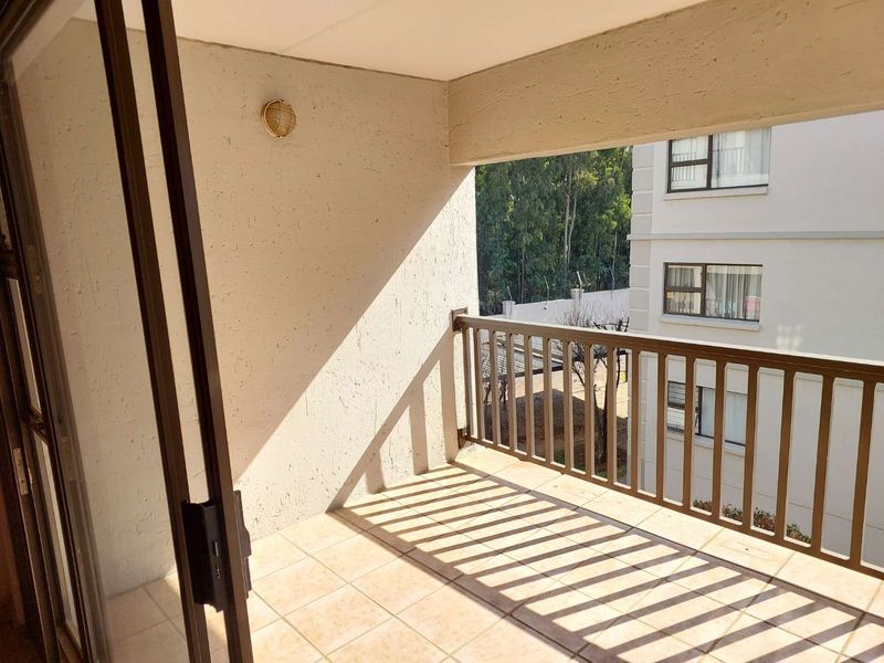 A covered balcony featuring tiled flooring and a metal balustrade, offering an open outdoor space accessible via a sliding glass door.