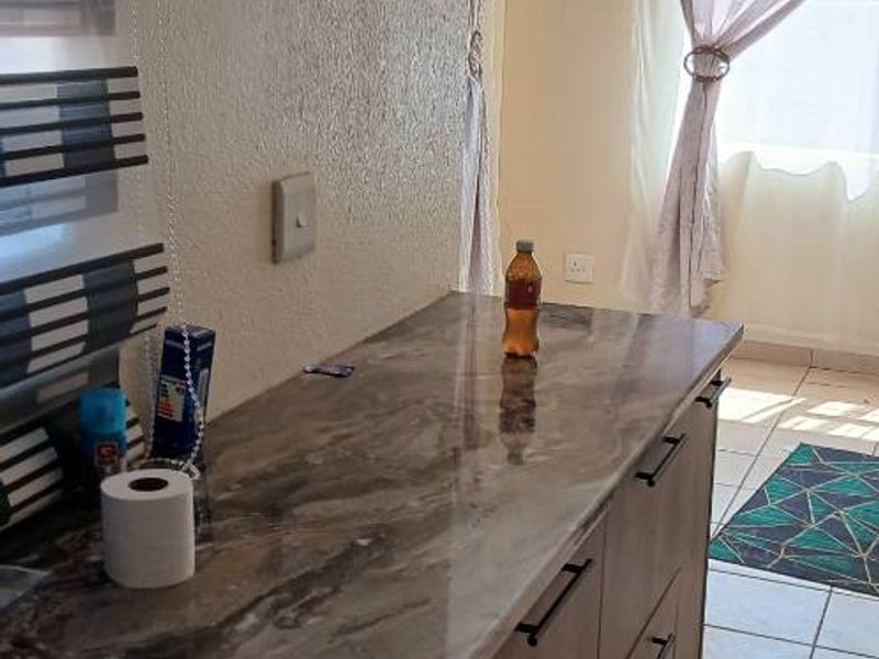 A functional kitchen area featuring modern marble-effect countertops, ample base cabinetry, and neutral ceramic floor tiles, offering a clean and practical workspace.