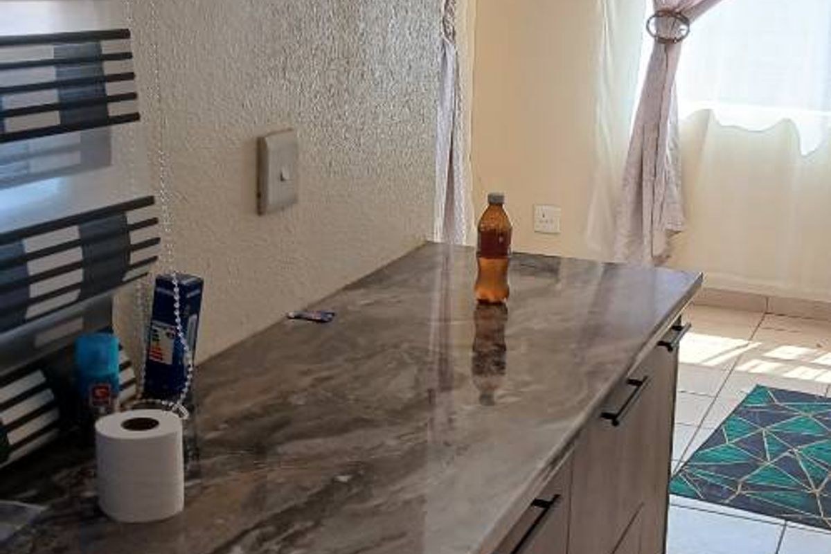 A functional kitchen area featuring modern marble-effect countertops, ample base cabinetry, and neutral ceramic floor tiles, offering a clean and practical workspace.