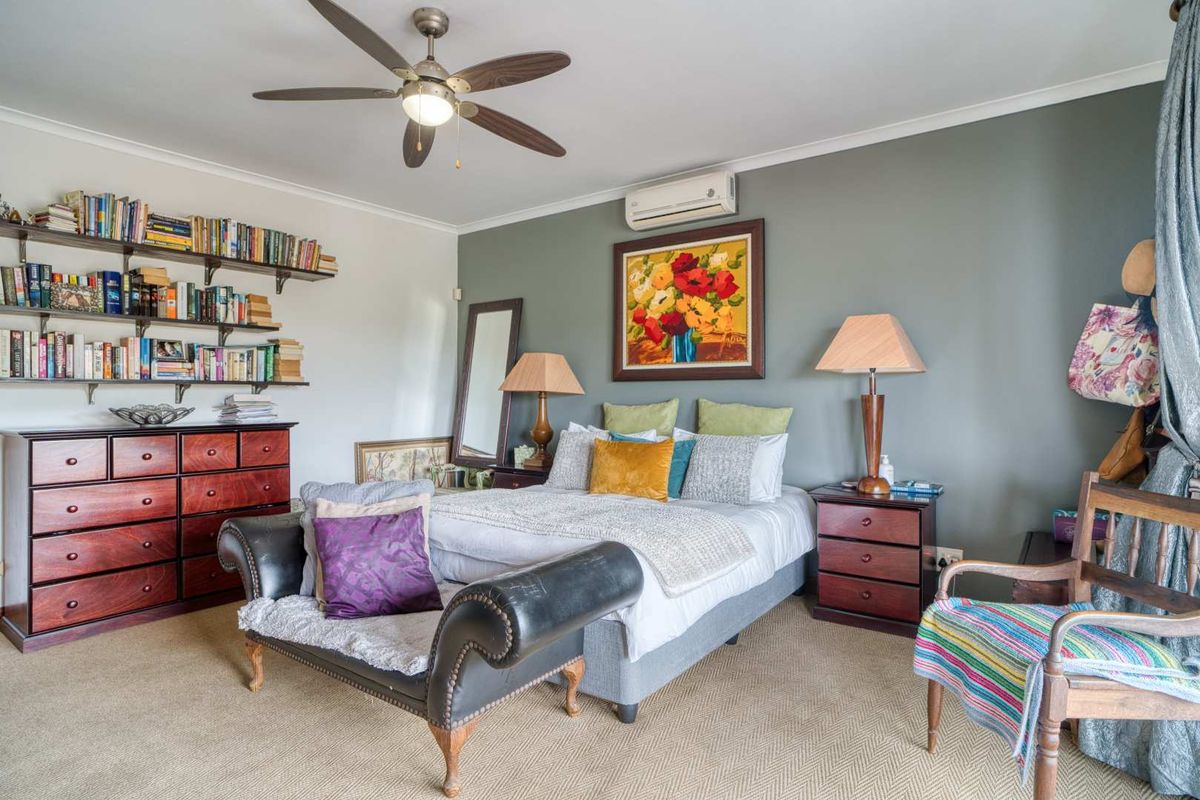 A well-maintained bedroom featuring a ceiling fan, wall-mounted air conditioning unit, and neutral carpeting.