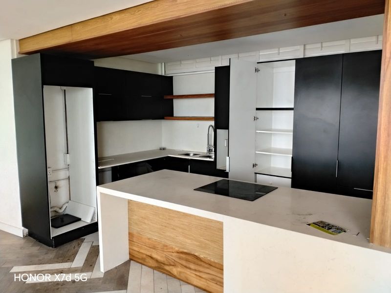Modern kitchen featuring a central island with integrated hob, stone countertops, two-tone cabinetry, and herringbone flooring. The space is currently undergoing final finishing touches.