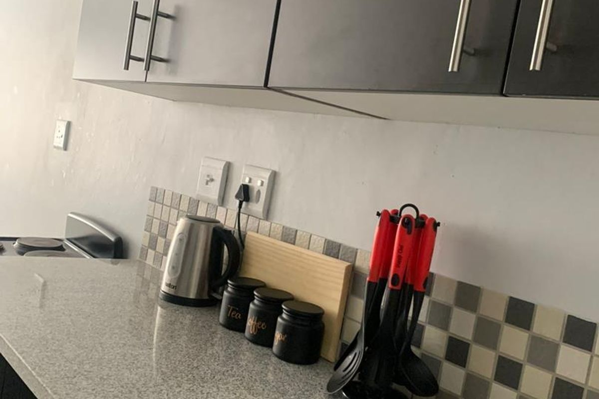 A functional kitchen area featuring granite countertops, mosaic tile backsplash, and modern dark grey cabinetry with stainless steel hardware.