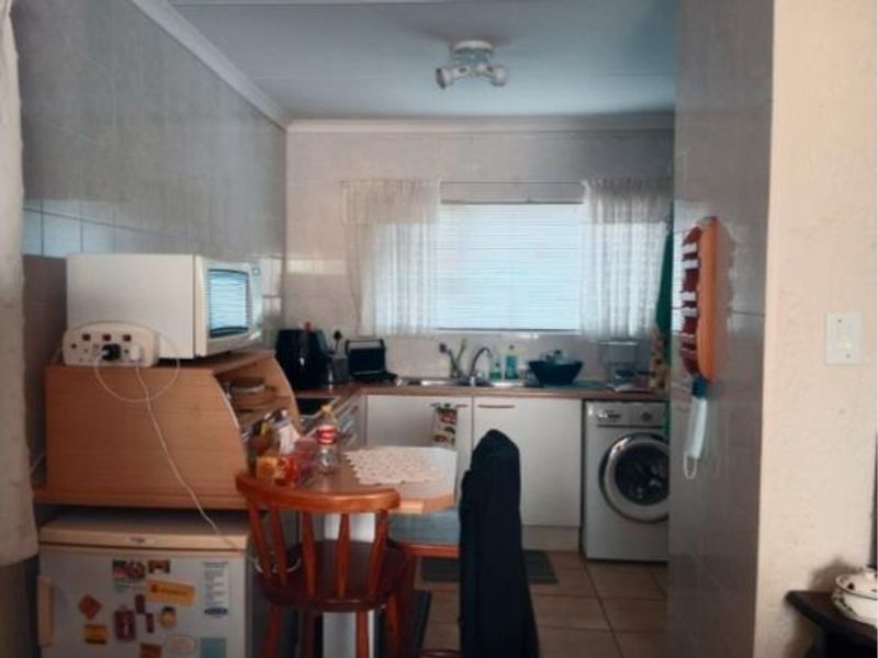 A functional kitchen featuring tiled walls and flooring, built-in cabinetry, a stainless steel sink, and space for a washing machine.